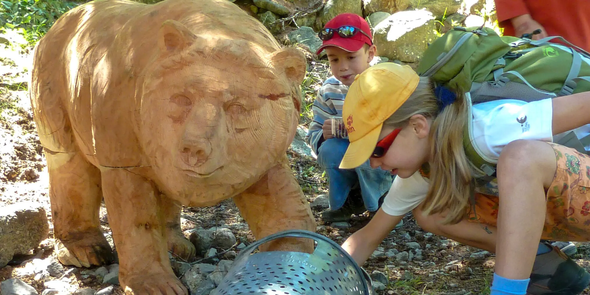 Kinder neben geschnitztem Holzbären mit der Atrappe eines Kehrichtkübels