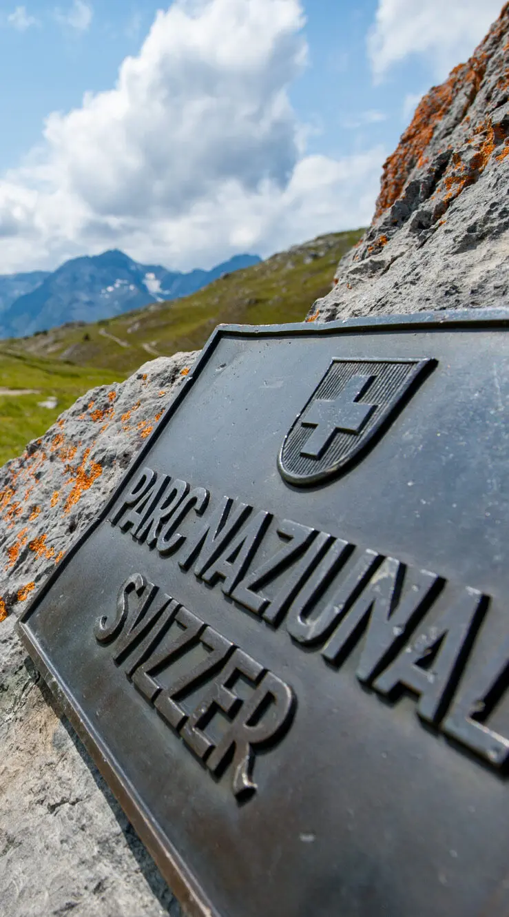 Metallschild Parc naziunal svizzer auf Steinbrocken am Wanderweg