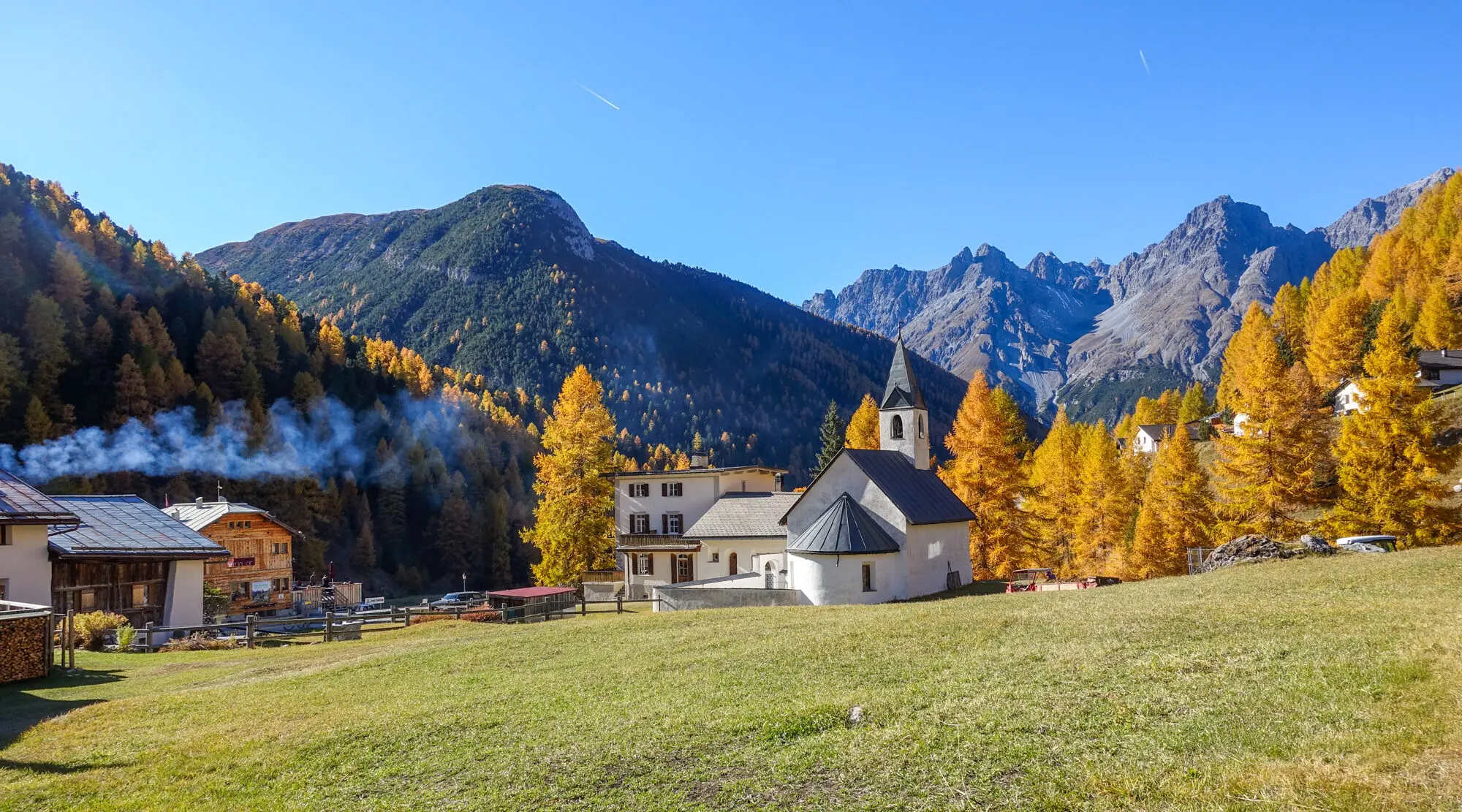 Herbstlandschaft im Ort S-charl, mit Kirche im Vordergrund und gelben Lärchen daneben